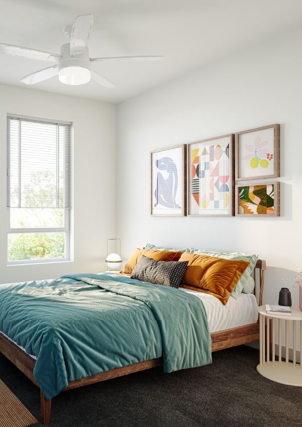 Wixby House Bright bedroom with a made bed, teal blanket, pillows, colorful wall art, window, and ceiling fan.